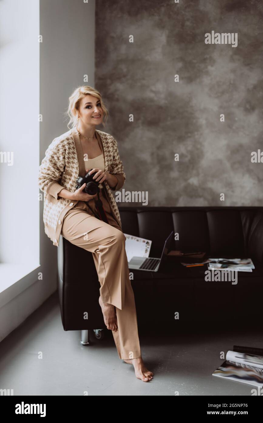 Joven hermosa mujer blogger en un moderno loft interior. Mujer fotógrafa  independiente con ropa beige sonriendo con una cámara en sus manos.  Selección suave Fotografía de stock - Alamy