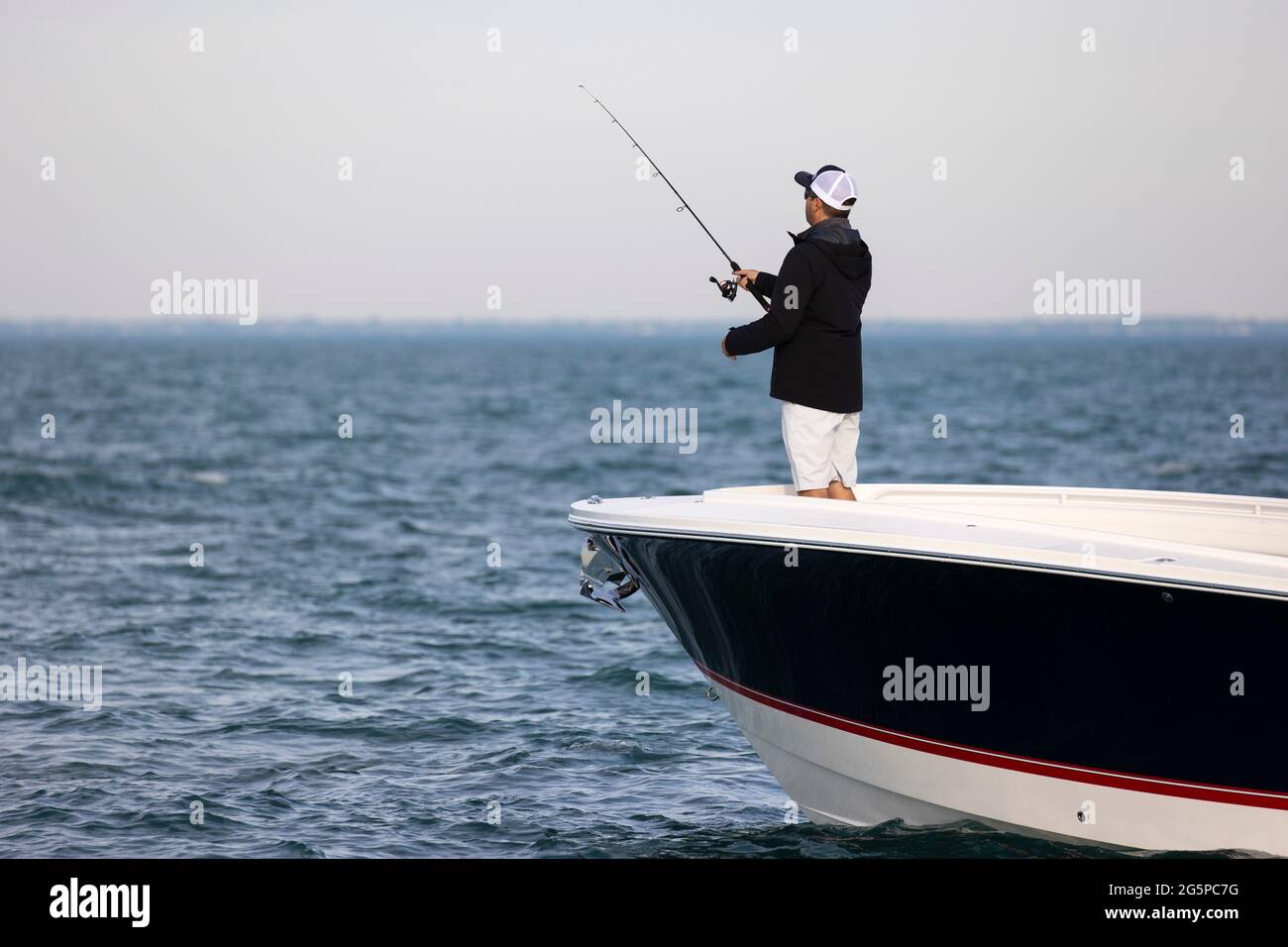Hombre pescando desde el arco de un barco en un lago vacío. Foto de stock