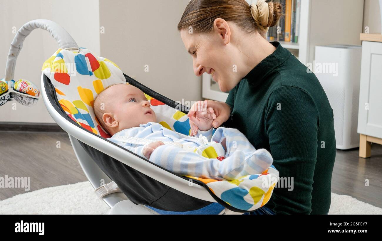 Retrato de una madre sonriente sentada junto al bebé hijo meciendo en un balancín  eléctrico. Desarrollo infantil y niñez Fotografía de stock - Alamy