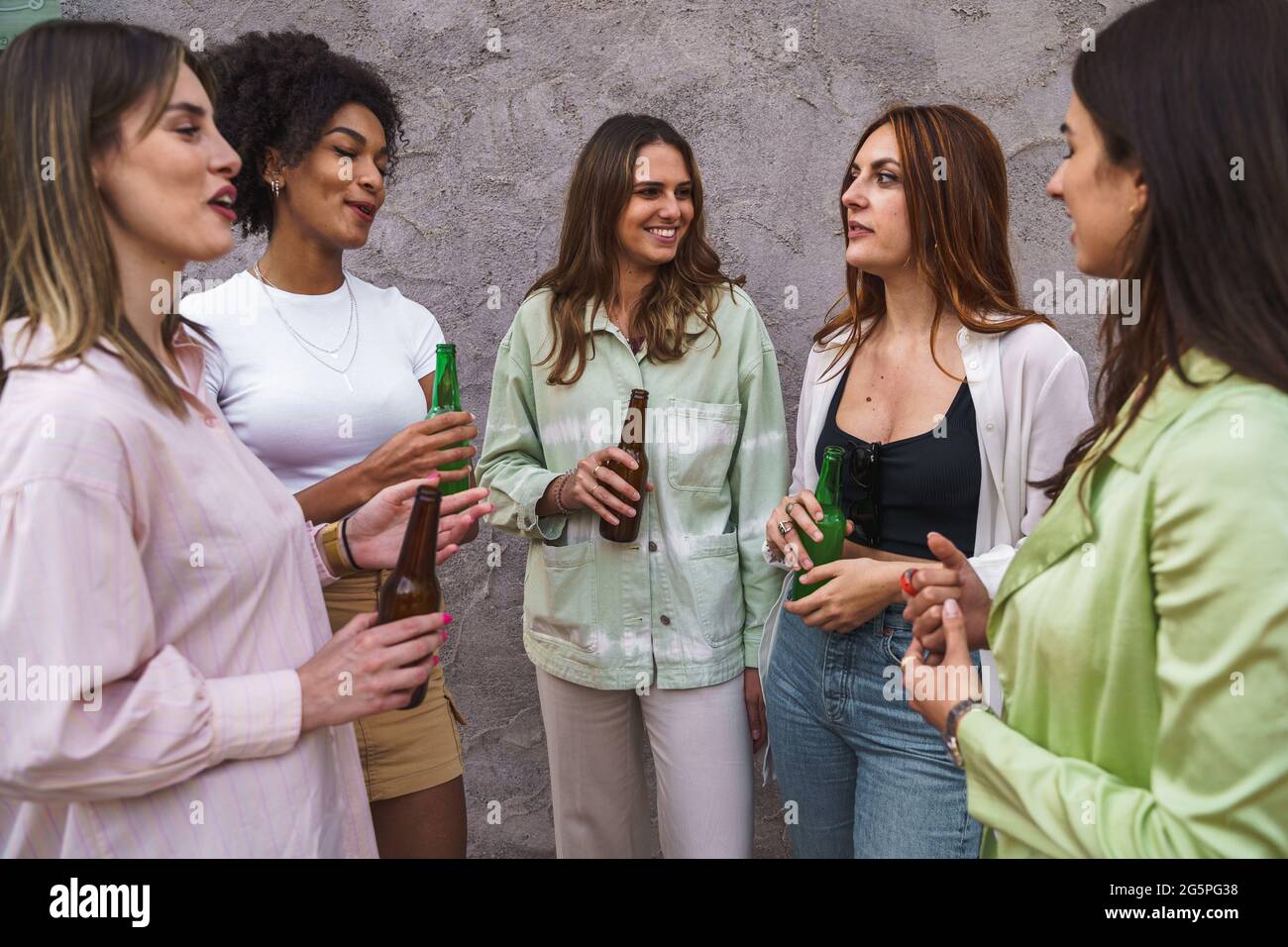 Mujeres de pie contra una pared hablando juntas y bebiendo cervezas. Concepto de comportamientos juveniles. Foto de stock