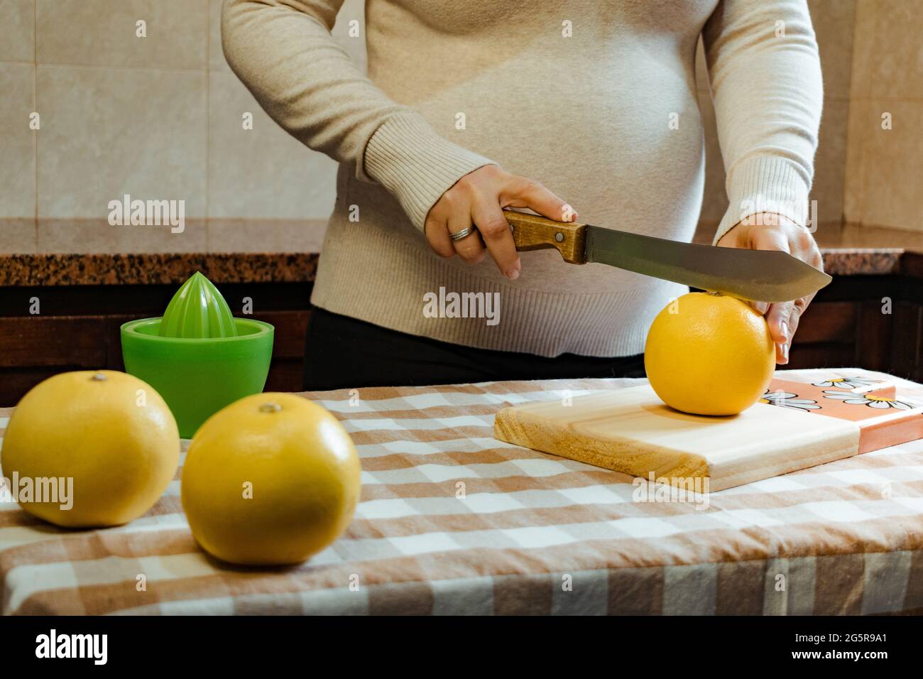 Las manos de una mujer latina embarazada cortando un pomelo por la