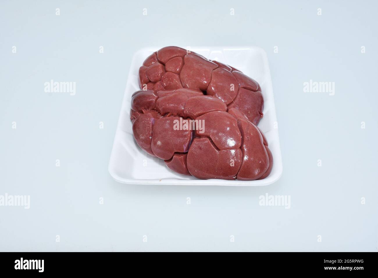 riñón de cordero fresco aislado en plato sobre fondo blanco, carne cruda closeup, pedazo de carnero Foto de stock