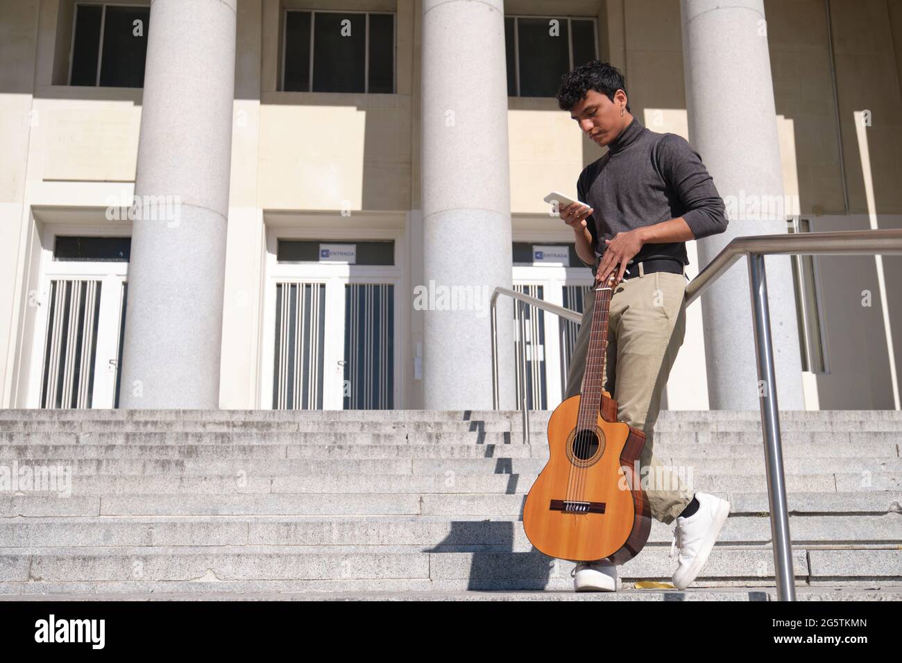Joven latino charlando en su smartphone con una guitarra en las escaleras.  Esperando algo Fotografía de stock - Alamy