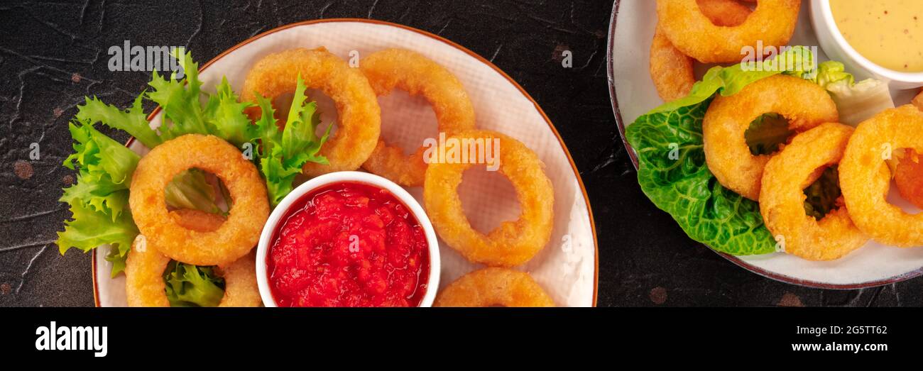 Panorama de los anillos de calamares. Anillos de calamares fritos profundos con ensalada verde y varias salsas, la parte superior plana se disparó sobre un fondo oscuro Foto de stock