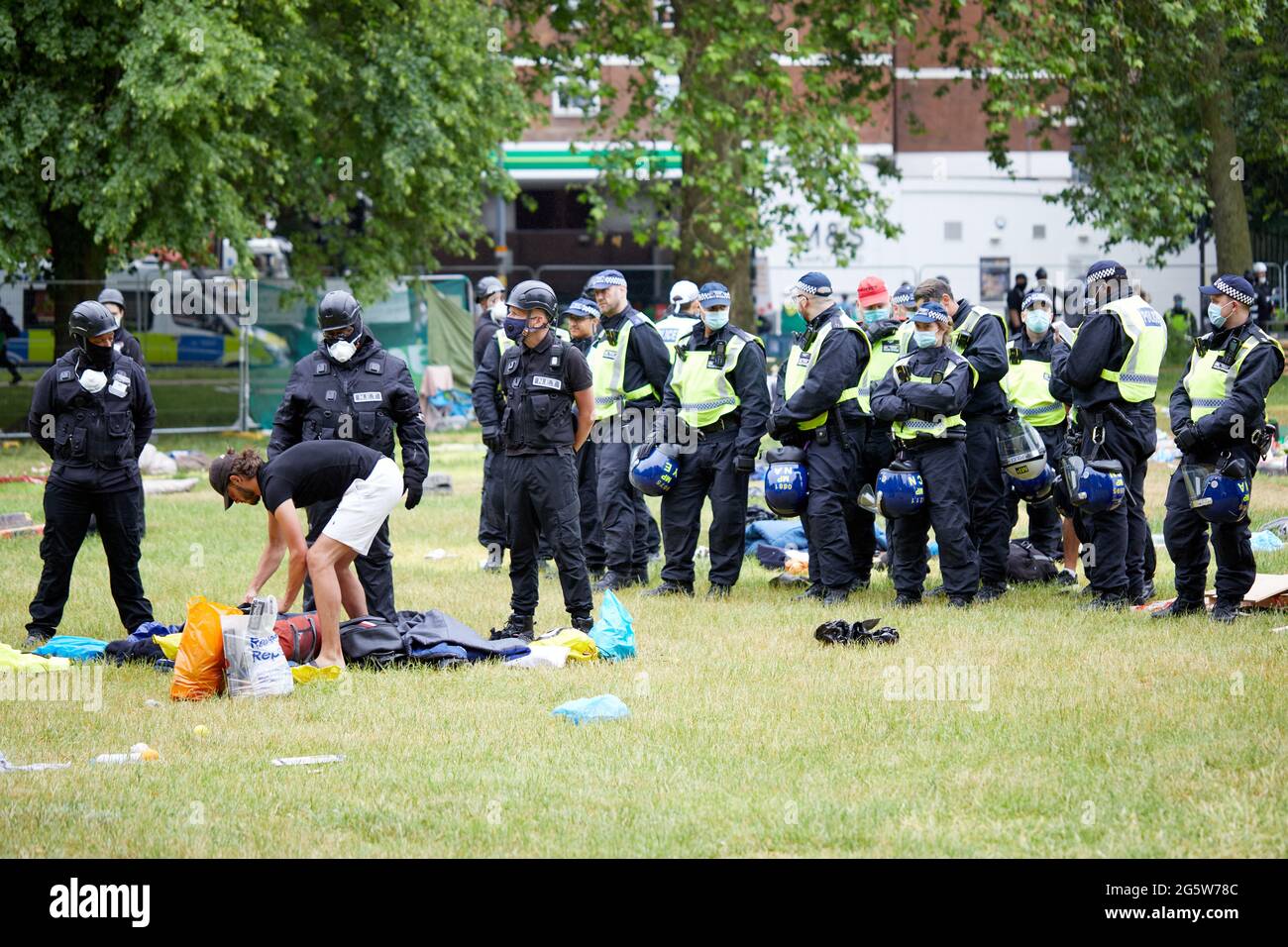 Londres, Reino Unido - 17 de junio de 2021: Los Baliffs esperan a que un manifestante embale sus pertenencias, vigilados por un gran número de policías, durante el desalojo del amoroso campo anti-encierro en Shepherds Bush Green. Foto de stock