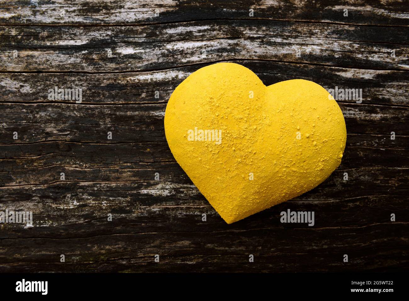 forma de corazón de 3 dimensiones pintada de amarillo, y rociada con pigmento seco, sobre el fondo de madera envejecida. Foto de stock