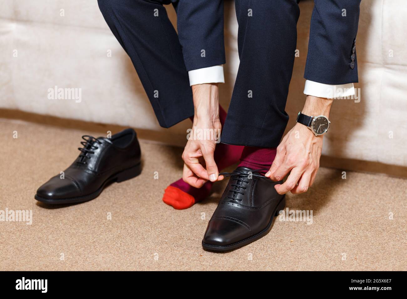 Un hombre de negocios con traje azul oscuro, calcetines rojos relojes atando sus cordones de zapatos negros. Moderno, elegante y caro para el hombre joven de stock - Alamy