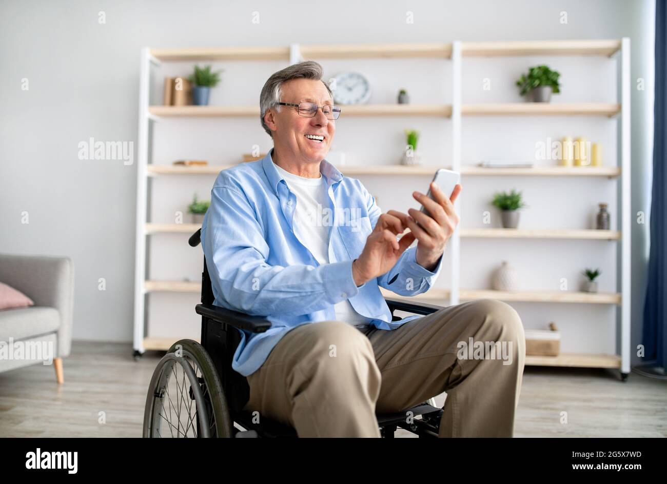 Feliz hombre mayor discapacitado en silla de ruedas usando el teléfono  móvil, navegando por la web o viendo una película en la casa de retiro  Fotografía de stock - Alamy