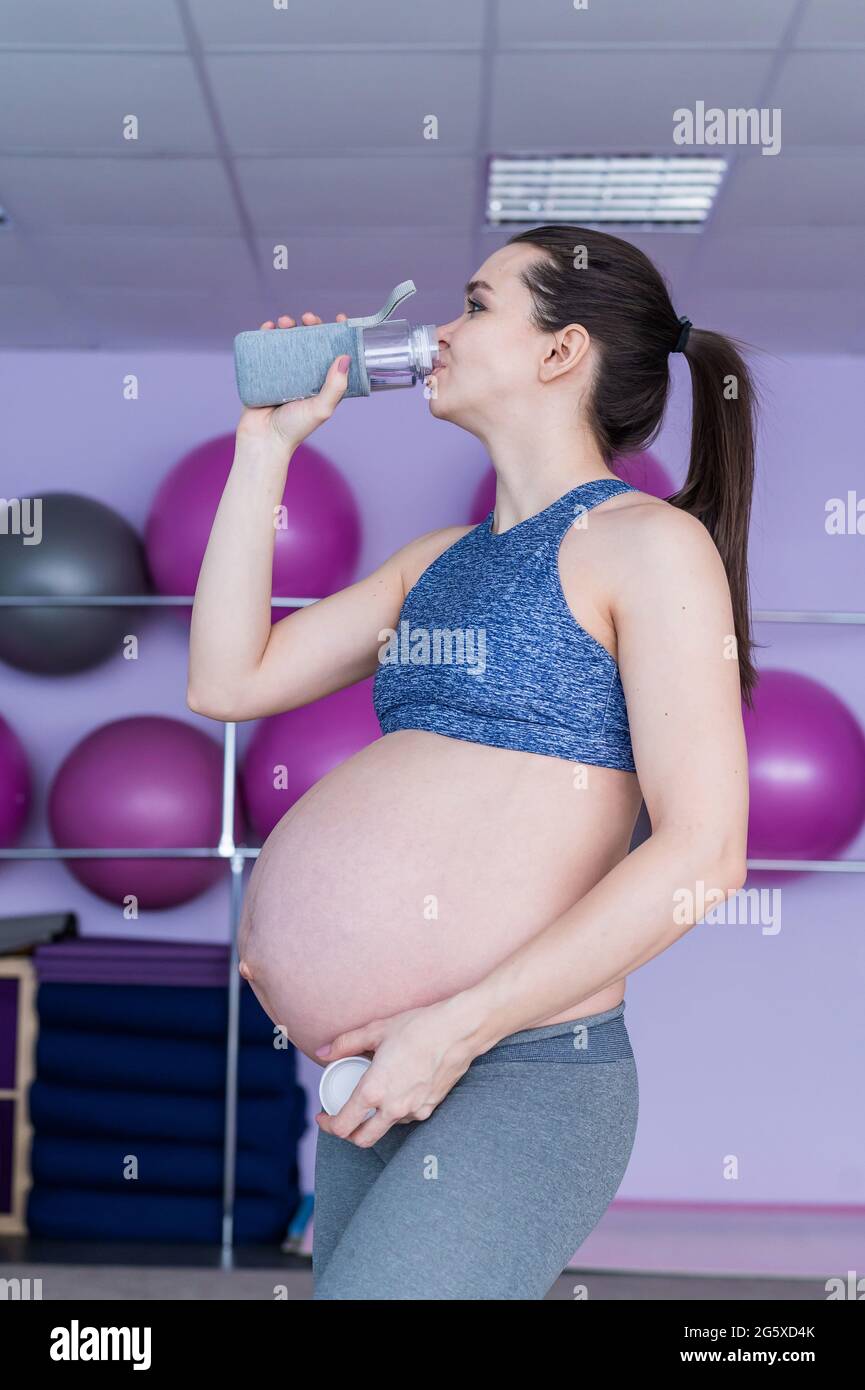 Una mujer embarazada en ropa deportiva bebe agua en el gimnasio con espadas  de fitness. La niña se dedica a Pilates para las mujeres embarazadas.  Último trimestre Fotografía de stock - Alamy
