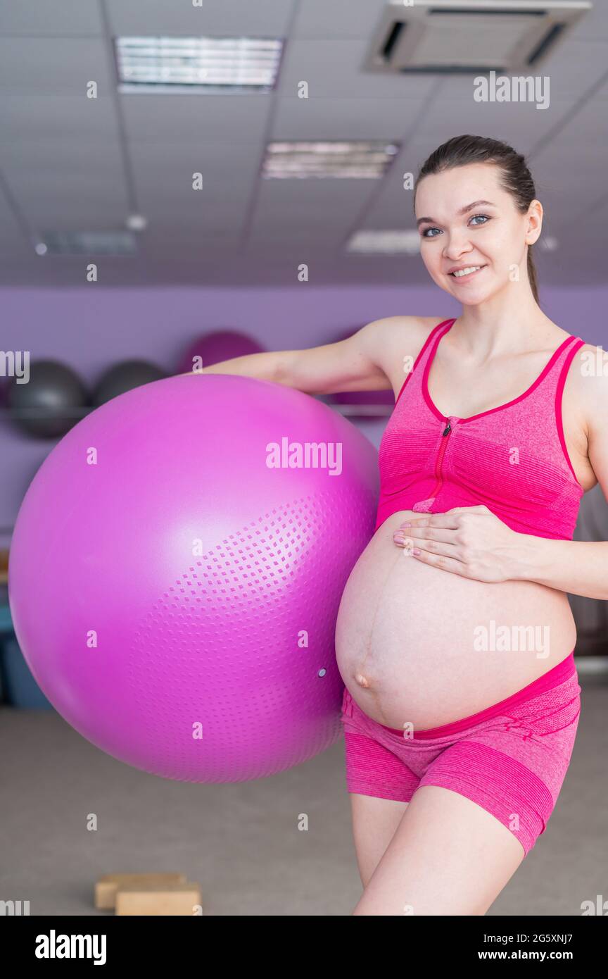 Una mujer embarazada en ropa deportiva está para las mujeres embarazadas. La chica se dedica a la forma física con una pelota para las mujeres embarazadas. Último Fotografía de stock -