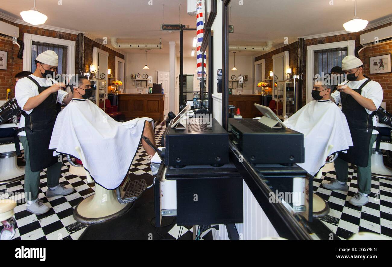 Toronto, Canadá. 30th de junio de 2021. Un barbero que usa una máscara facial corta el cabello de un cliente en un salón de belleza en Toronto, Ontario, Canadá, el 30 de junio de 2021. La provincia canadiense de Ontario permitió que la mayoría de las regiones reabrieran más negocios el miércoles a medida que se trasladaban al segundo paso del plan de reapertura de la provincia, incluyendo salones de cabello, salones de uñas y tiendas en centros comerciales. Crédito: Zou Zheng/Xinhua/Alamy Live News Foto de stock