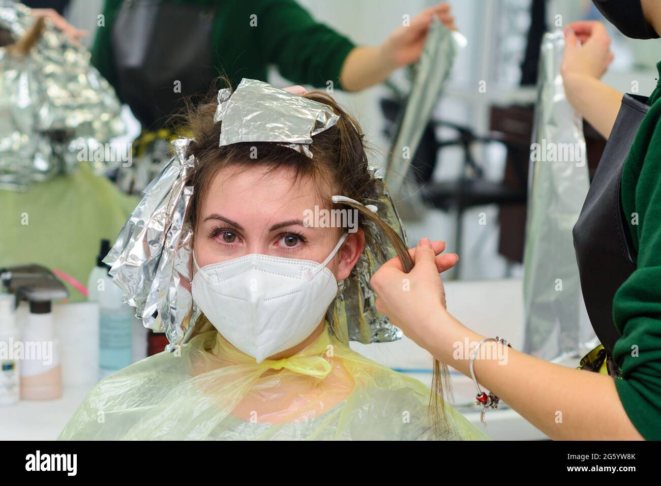 El peluquero se tiñe el cabello femenino, haciendo que el cabello de su  cliente se destaque con un papel de aluminio.