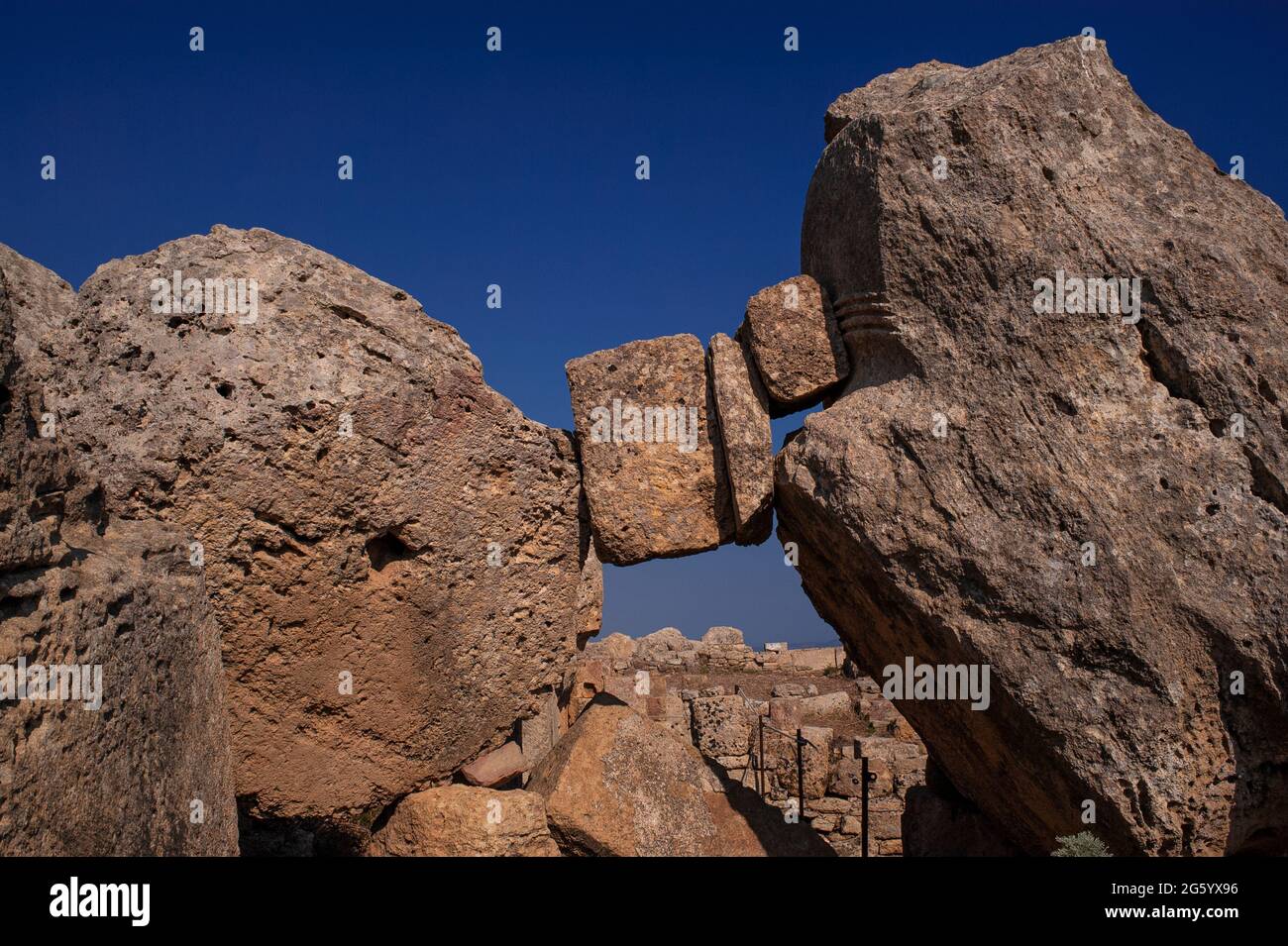 Colgando en el espacio y el tiempo en Selinunte, Sicilia, Italia: Pedazos de la mampostería griega antigua atrapados donde cayeron entre un tambor de columna inacabado y un corte parcial de la capital dórico de la roca sólida, en medio de las columnas caídas y otros trabajos de piedra de un templo derrumbado dedicado a Apolo o Zeus en la ciudad de Selinus o Selinous. La estructura, ahora conocida como Templo G, es el segundo templo griego más grande de Sicilia. Fue fundada en el año 530 a.C. pero estaba incompleta cuando Cartago saqueó a Selinus en el año 409 a.C. Más tarde colapsó, probablemente en un terremoto medieval. Foto de stock