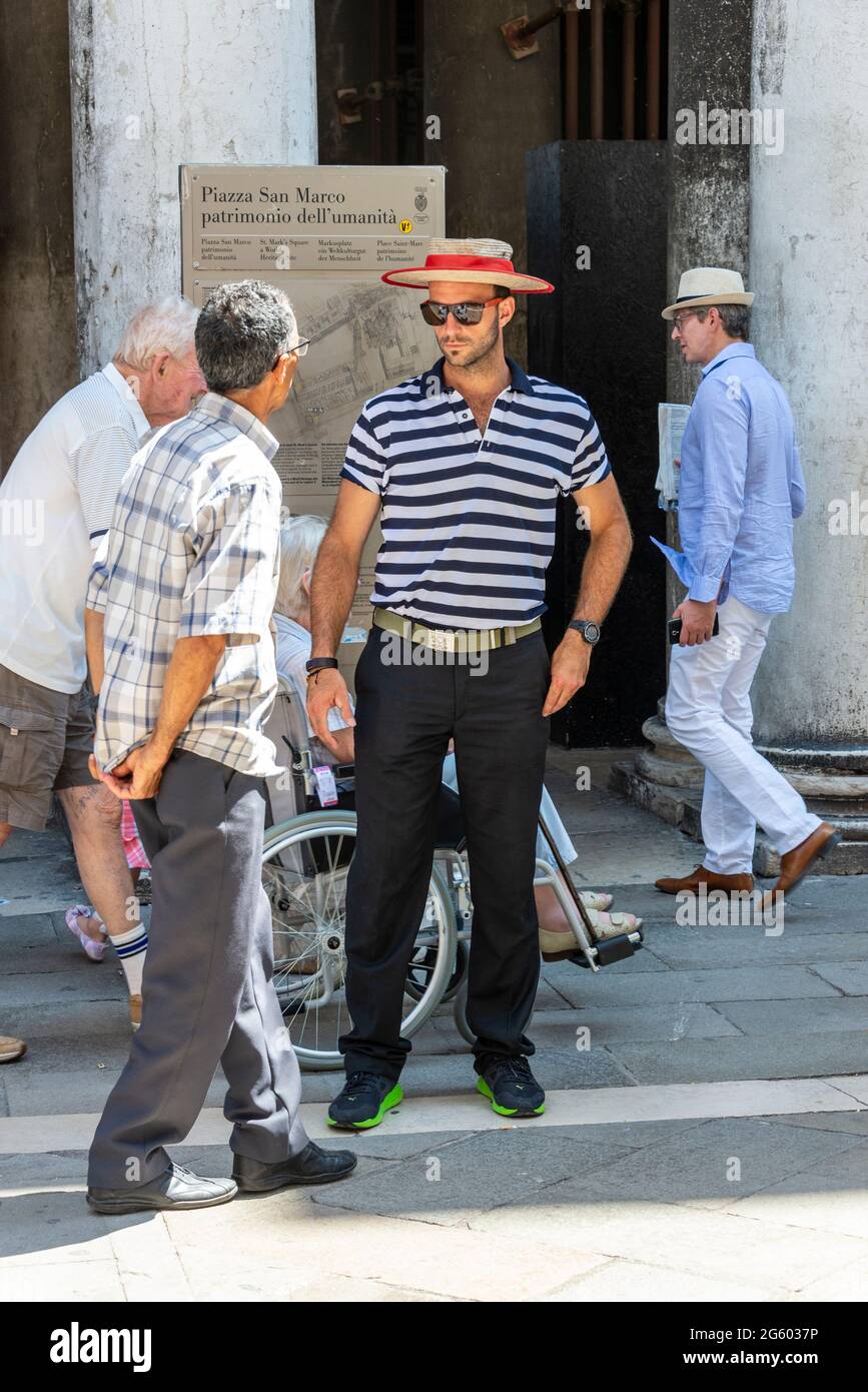 Un gondolero que lleva su tradicional camisa azul y blanca a rayas y un  boater con una diadema roja, que se anuncia para los negocios en Venecia,  norte de Italia Fotografía de