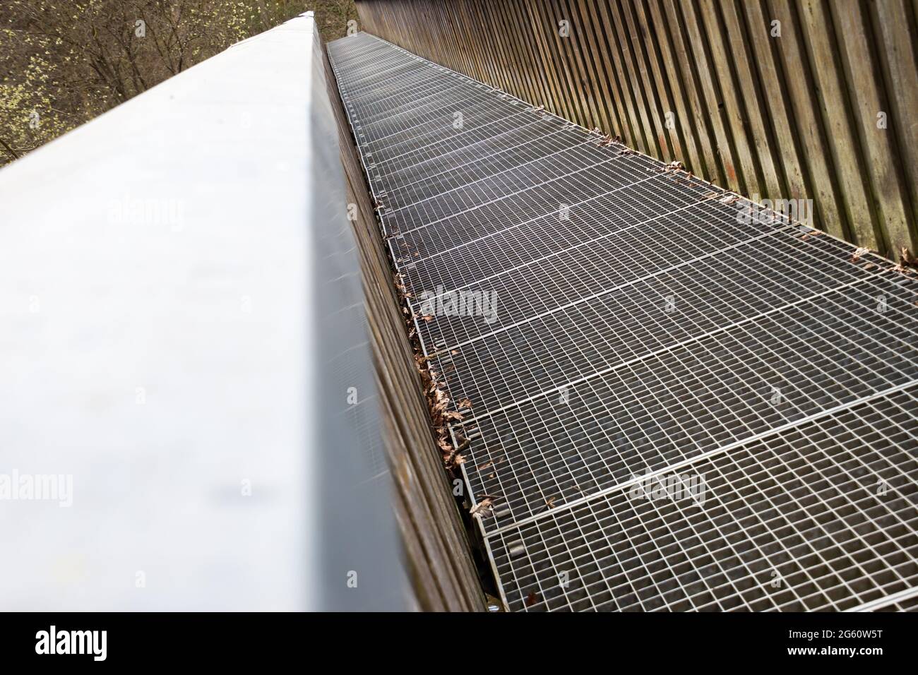 Puente de pie con suelo de rejilla de hierro y barandilla de madera que cruza un río Foto de stock