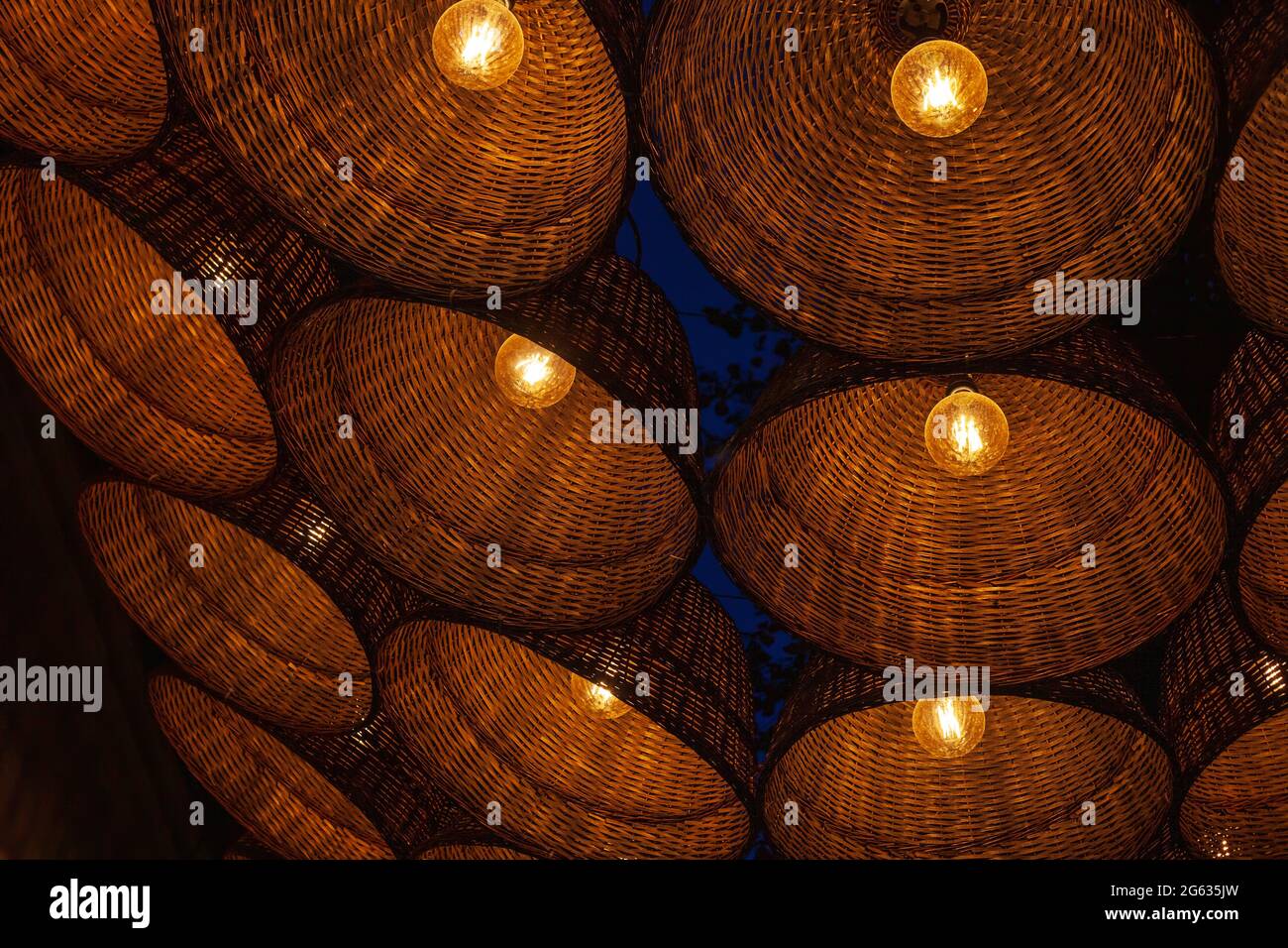 Muchas luces de mimbre cuelgan por el fondo del cielo nocturno oscuro. Gran cantidad de linterna eléctrica colgante, decoración festiva en el patio de la noche Foto de stock