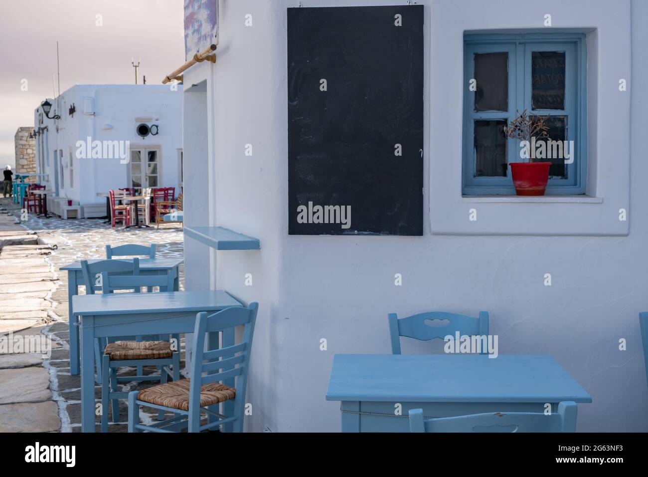 Tradicional cafetería y taberna al aire libre. Grecia, puerto antiguo de  Naousa, pueblo pesquero griego en la isla de Paros. Mesas y sillas vacías  azules, blackboar en blanco Fotografía de stock -