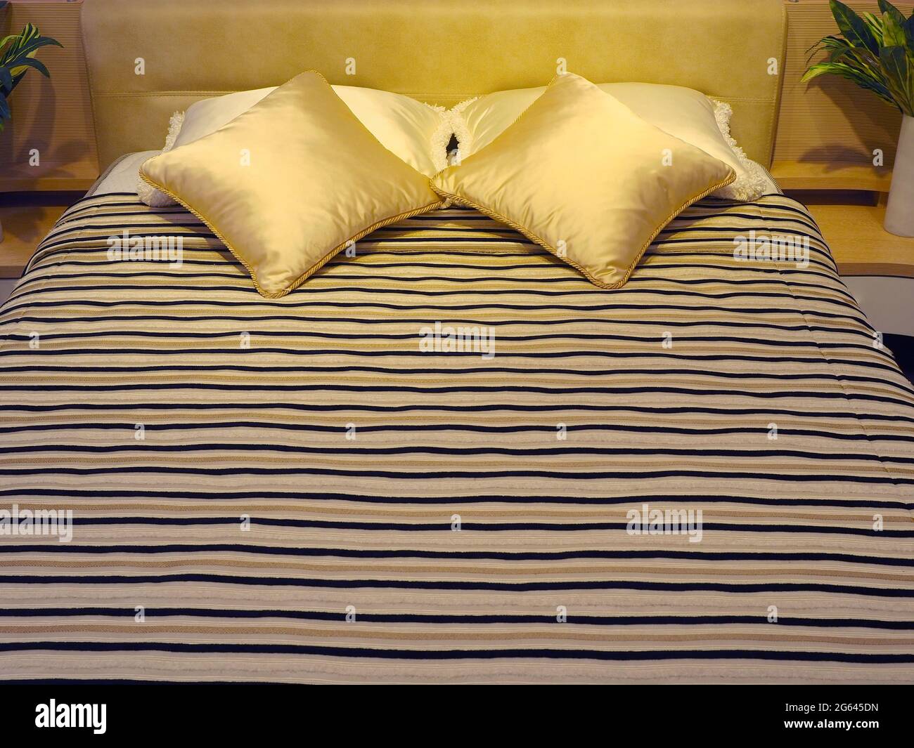 Cama con cabecera tapizada, almohadas de seda decorativa cuadrada y edredón  a rayas Fotografía de stock - Alamy