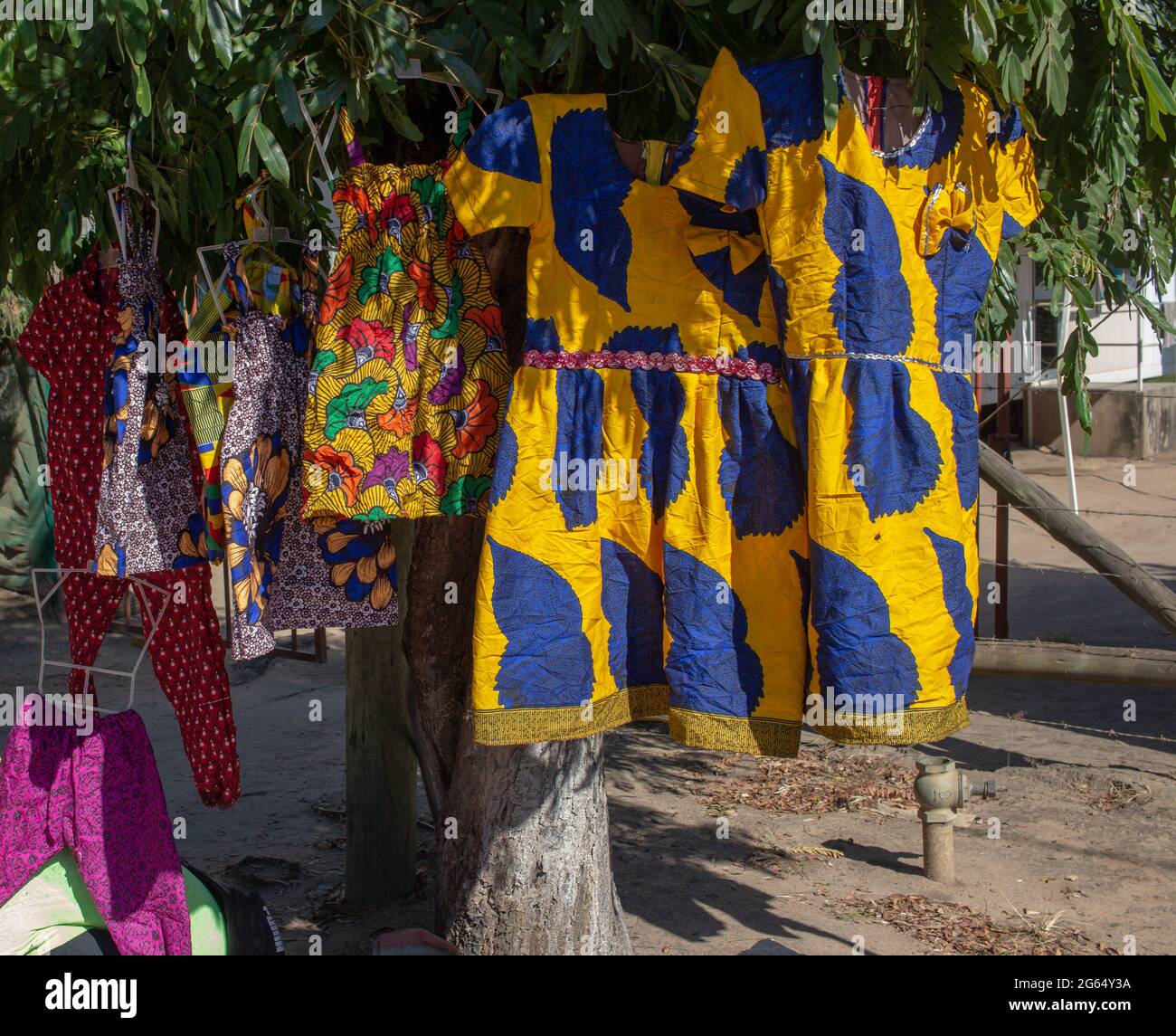 Vestidos y trajes hechos de telas tradicionales exhibidos en un árbol en la calle para la venta Fotografía de stock -