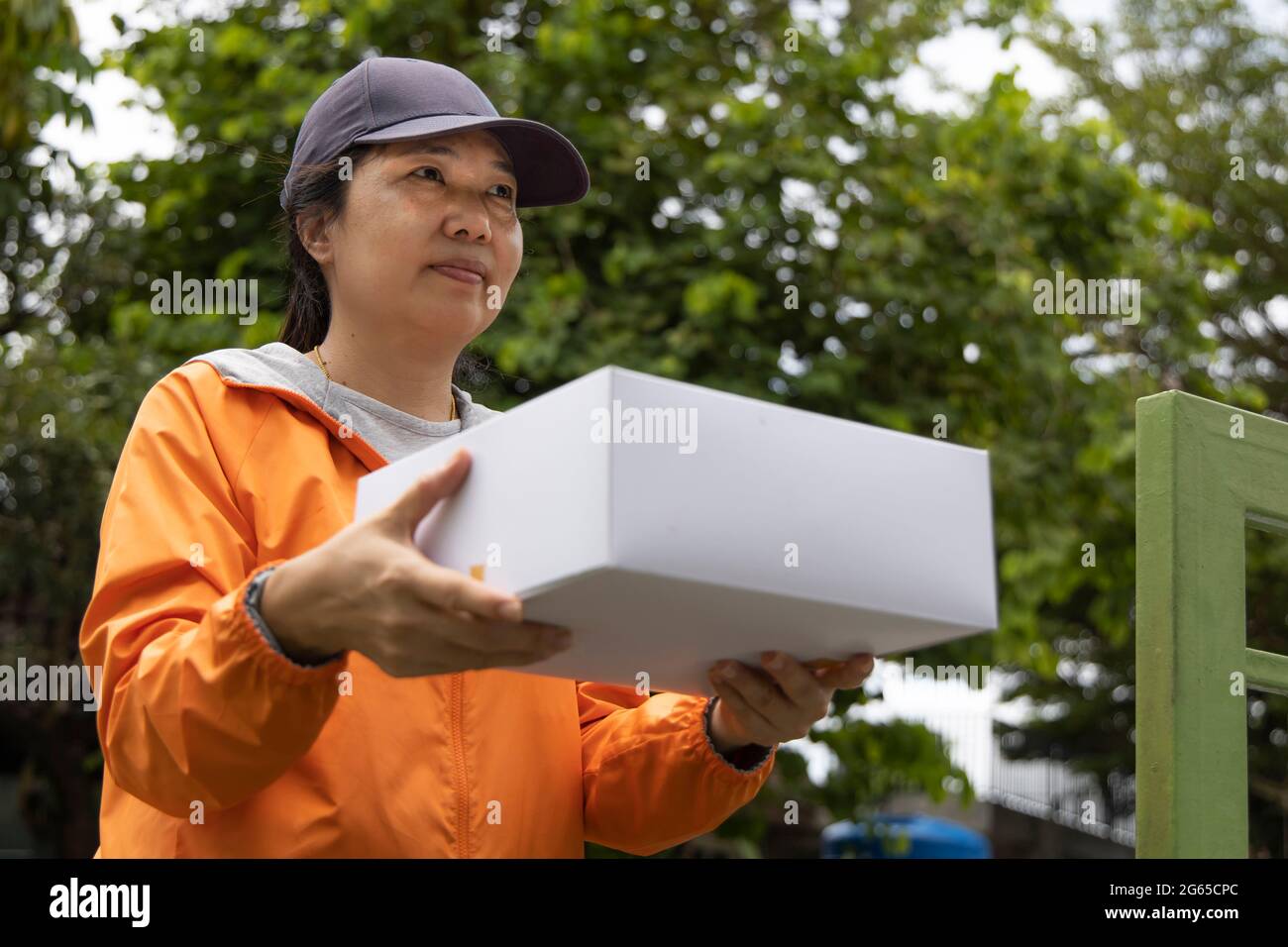 Una empleada que llevaba una bata naranja entregó un regalo en una caja blanca al frente de la casa. Foto de stock