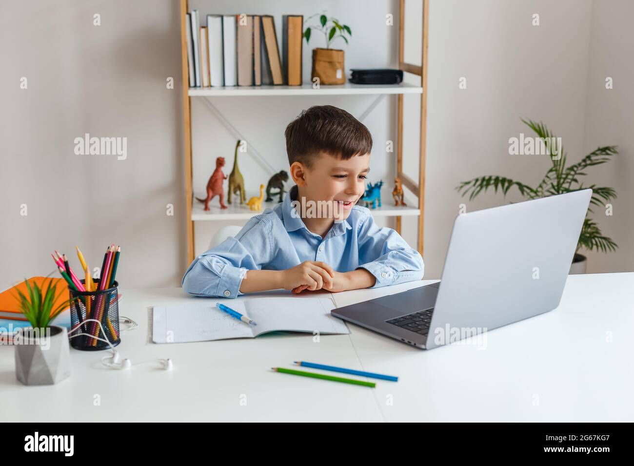 Niño a través del portátil hablando con el profesor durante el estudio en línea en casa. E-learning en la escuela primaria mediante videollamada. Niño divertido haciendo la tarea con interno Foto de stock