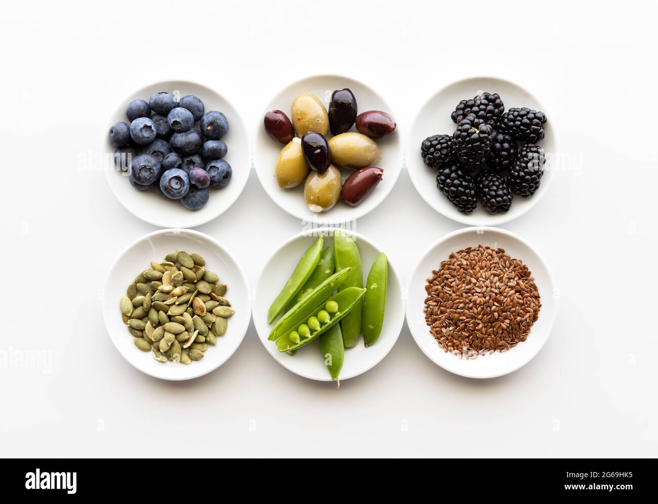 Vista de arriba abajo de una pequeña vajilla de varios ingredientes saludables incluyendo semillas, verduras, aceitunas y bayas. Foto de stock