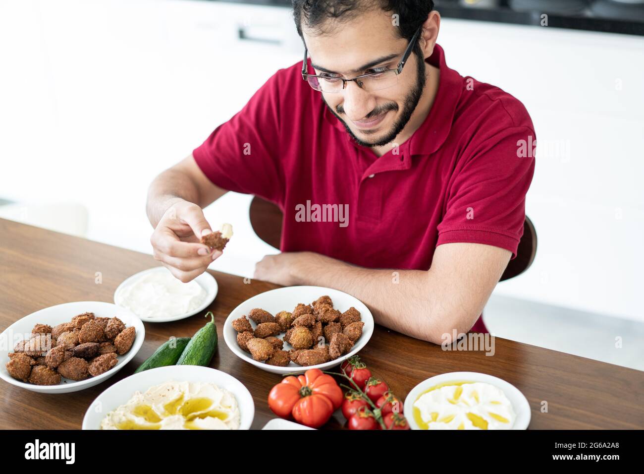 Joven de Oriente Medio sentado y comiendo comida tradicional sola Foto de stock