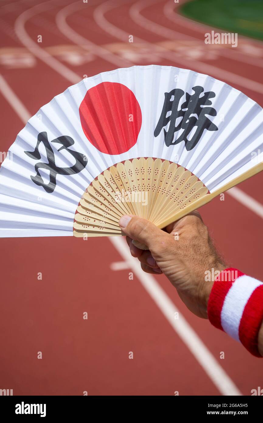 Mano de atleta deportivo japonés sosteniendo un ventilador decorado con caracteres kanji deletreando hissho, cierta victoria en inglés en una pista de carreras Foto de stock