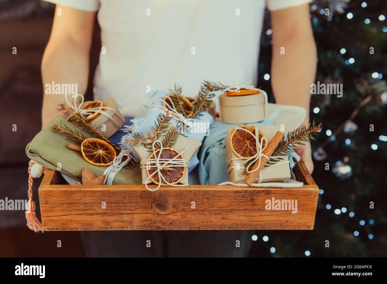 Hombre sosteniendo una bandeja de madera con cajas de regalo de Navidad  envueltas ecológicas decoradas con naranja natural seca, canela y rama de  picea. Cristo Fotografía de stock - Alamy
