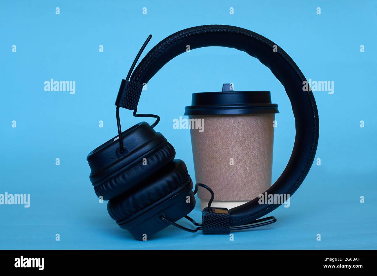 Una taza de papel para café y auriculares inalámbricos sobre un fondo azul. Foto de stock