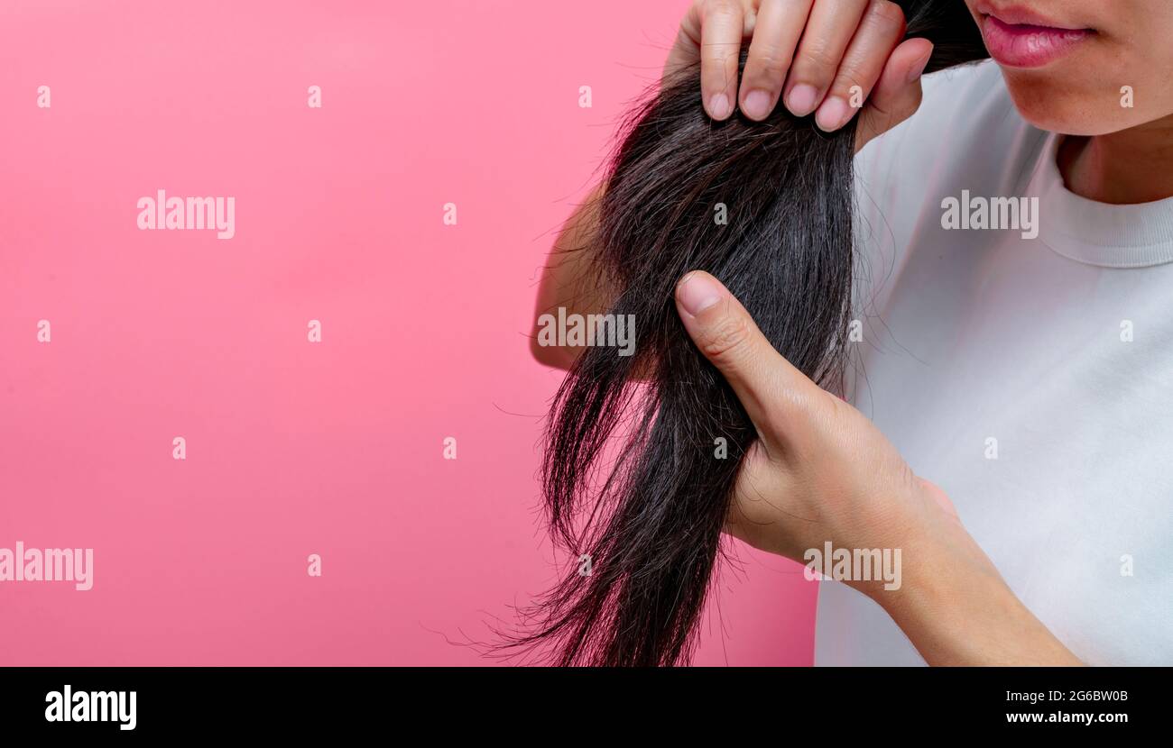 Mujer asiática con labios secos sosteniendo el cabello dañado sobre fondo  rosa. El cabello largo negro seco y frágil necesita champú y acondicionador  para el tratamiento de spa Fotografía de stock -