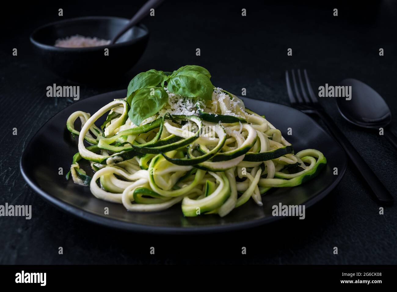 Fideos, fideos de calabacín con parmesano y albahaca sobre un plato negro sobre fondo negro. Para bajo carb, keto, vegetariano, paleo nutrición y dieta. Foto de stock