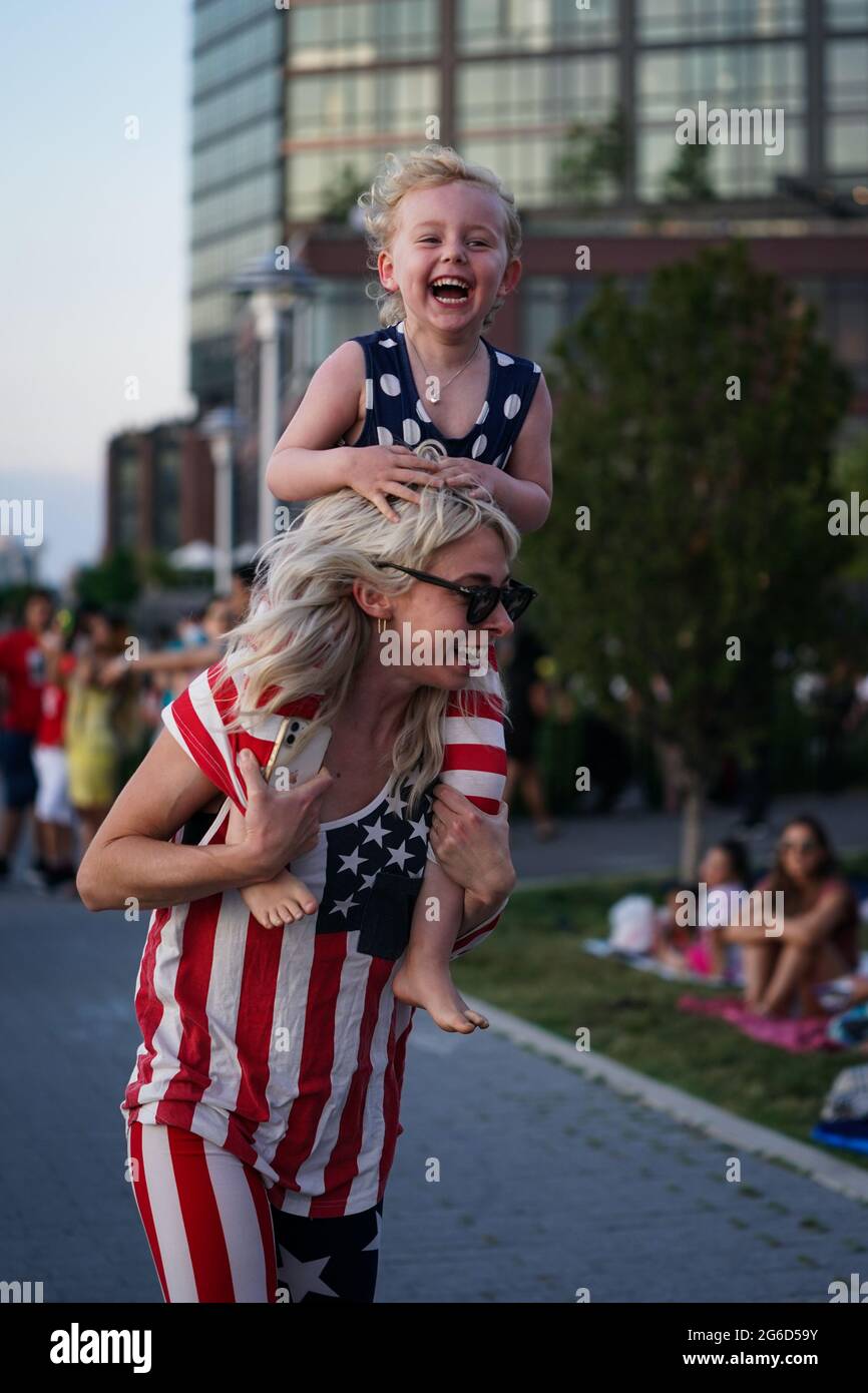 Nueva York, Estados Unidos. 4th de Jul de 2021. Una joven se ríe mientras estaba sobre los hombros de su madre antes del espectáculo de fuegos artificiales del 4 de julio de Macy en Nueva York, Estados Unidos. Crédito: Chase Sutton/Alamy Live News Foto de stock