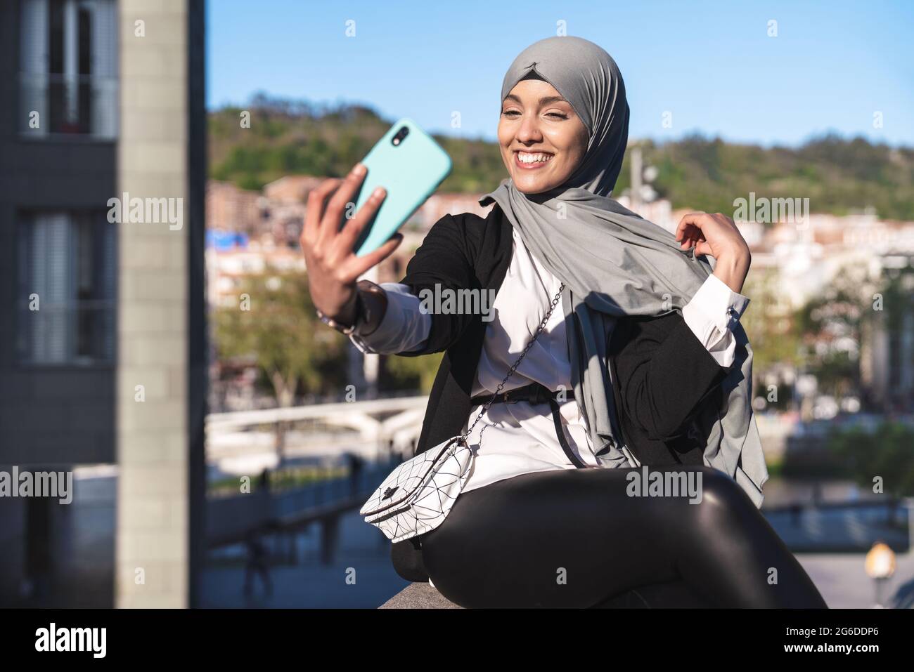 Foto Hermosa mujer musulmana con ropa formal y hiyab haciendo compras en  línea con tarjeta de crédito y teléfono inteligente. Joven de pie cerca del  edificio de oficinas y disfrutando de un