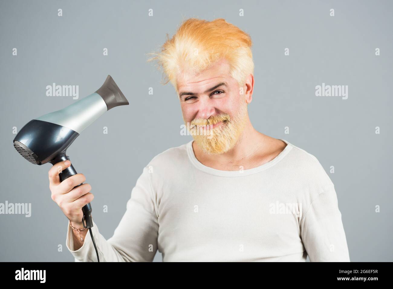 Rubia barba hombre cabello seco. Hombre joven secando el pelo con secador  de pelo Fotografía de stock - Alamy