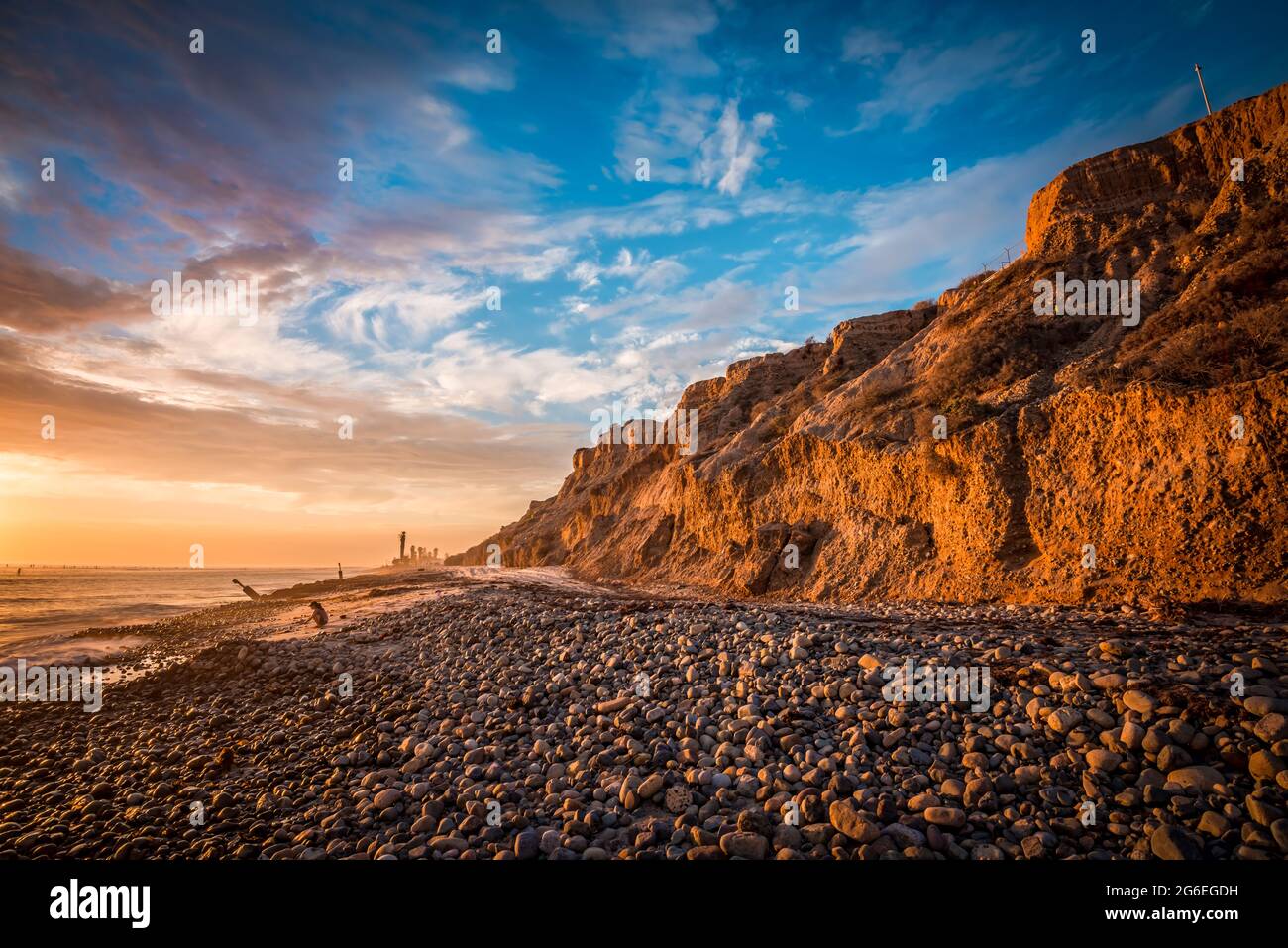 Hermosa puesta de sol en la playa con acantilados iluminados por el sol y una costa rocosa Foto de stock