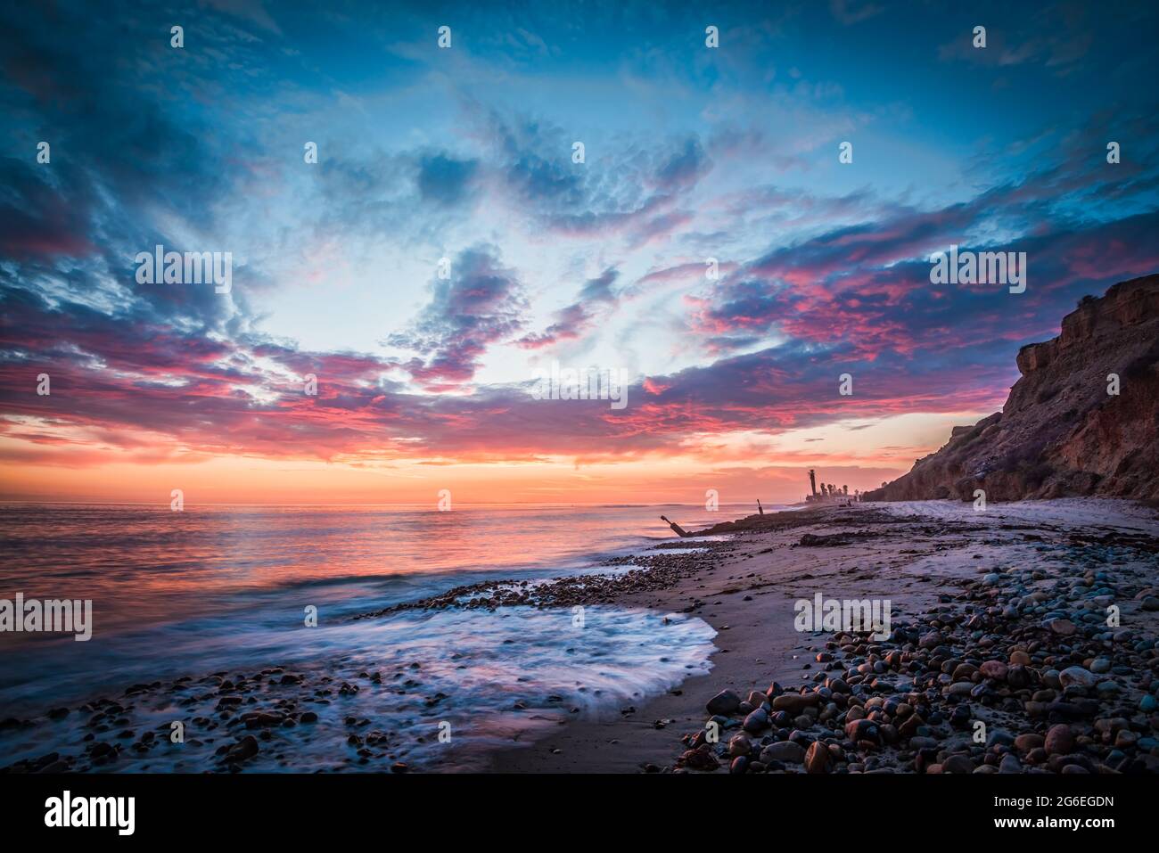 Hermosa puesta de sol en la playa con una costa rocosa Foto de stock