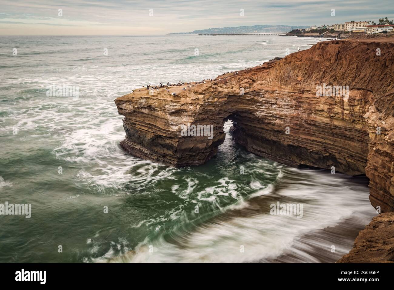 Olas de larga exposición rompiendo contra los acantilados de playa en un nublado día Foto de stock