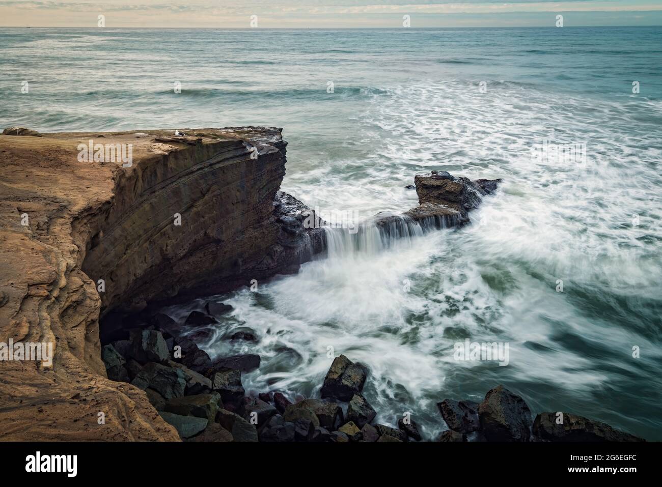 Olas de larga exposición rompiendo contra los acantilados de playa en un nublado día Foto de stock