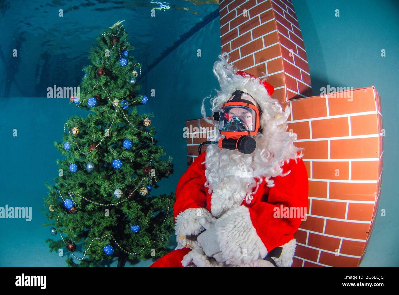 Imagen submarina de Santa Claus en el buceo con un árbol de Navidad y chimenea roja Foto de stock