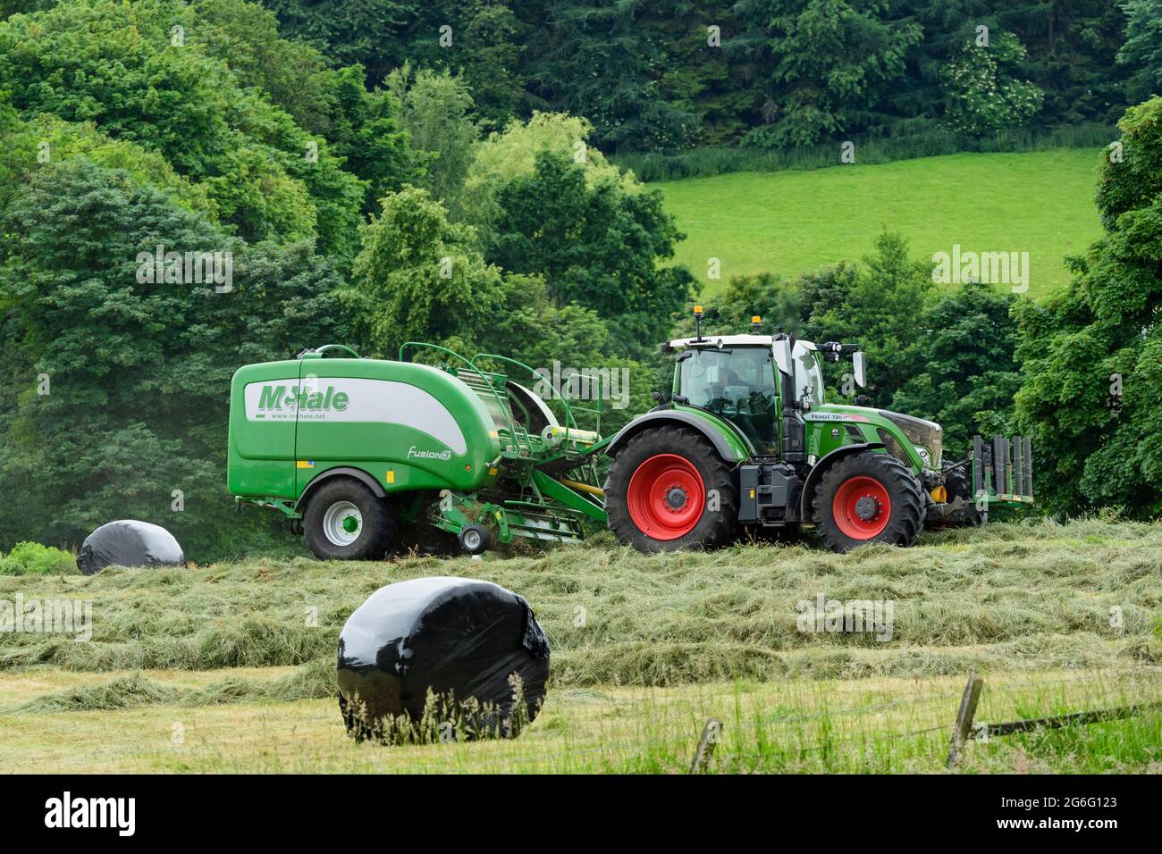 Fabricación de heno o ensilaje (agricultor en tractor agrícola en el trabajo en campo rural, tirando de empacadora, recogiendo césped seco y pacas redondas envueltas) - Yorkshire England Reino Unido. Foto de stock