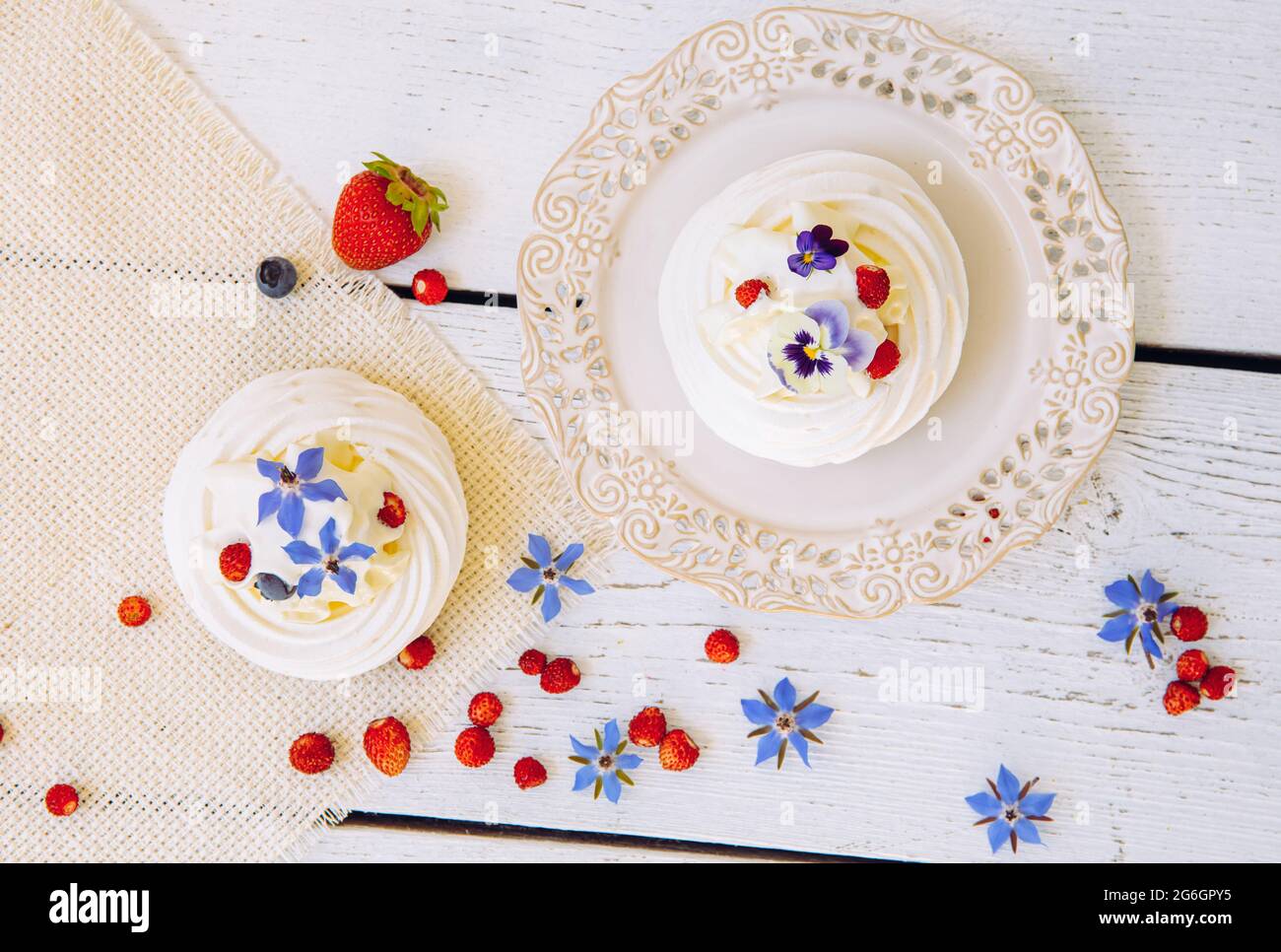 Pequeños pasteles de merengue, decorados con nata montada, bayas frescas y flores comestibles de la vida real. Foto de stock