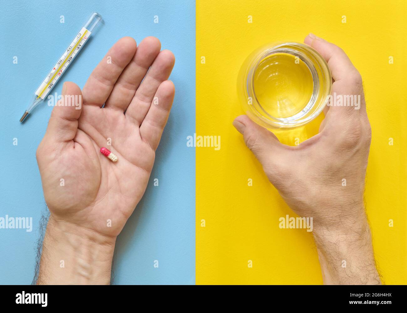 Tomando medicina, las manos del hombre sosteniendo una píldora y un vaso de agua, vista superior, fondo amarillo y azul Foto de stock