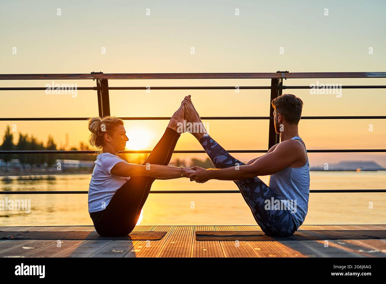 En forma pareja joven haciendo acro yoga en el muelle junto al mar. Estilo  de vida saludable. Actividades deportivas al aire libre para personas  durante las vacaciones familiares Fotografía de stock -