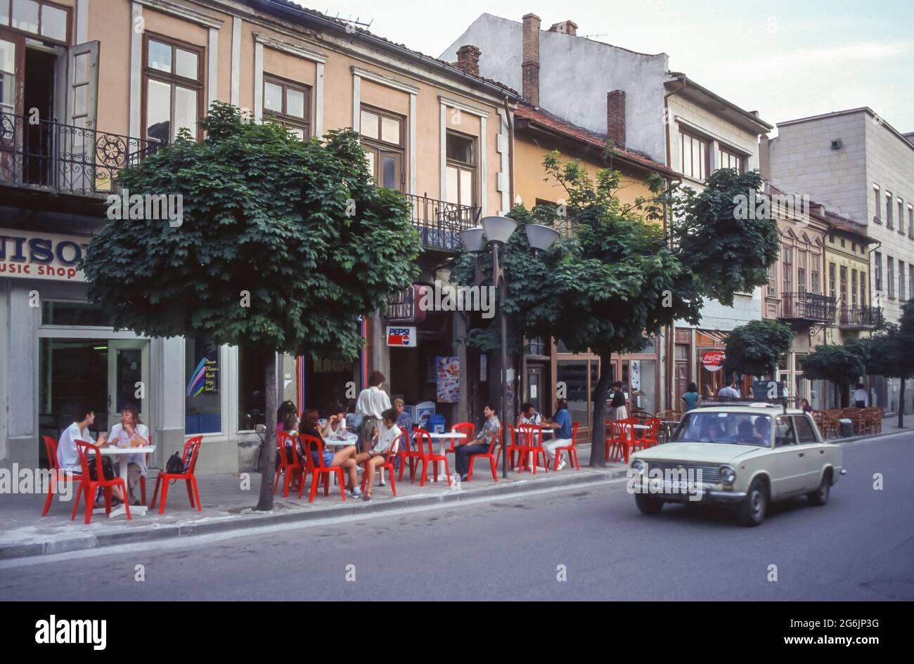 VELIKO TARNOVO, BULGARIA - El coche pasa al café al aire libre en la acera de la ciudad vieja en Veliko Tarnovo histórico. Foto de stock