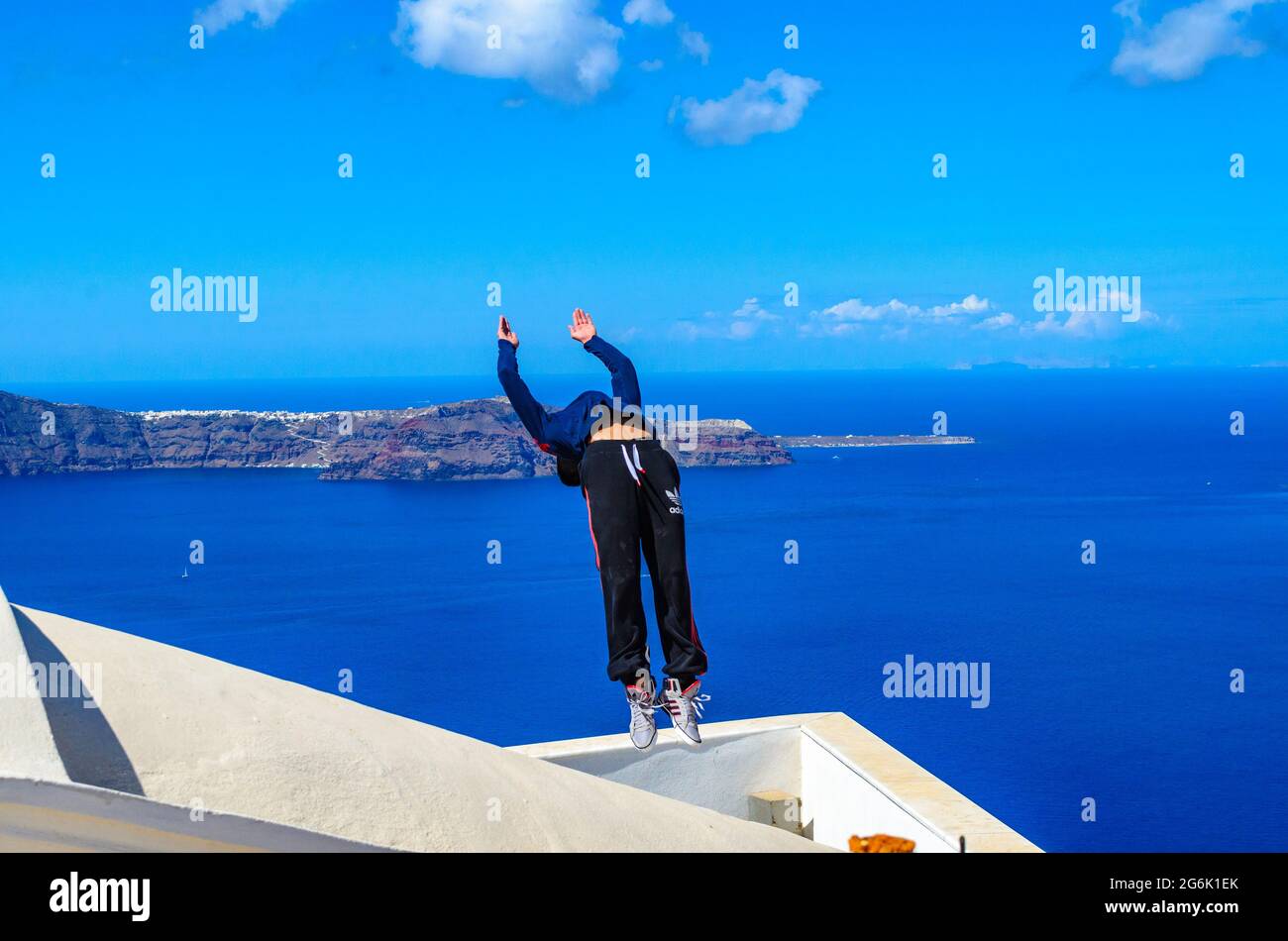 La espalda de un joven atleta se voltea durante el Parkour y el Free Running. Atleta profesional que realiza un backflip en un techo en Santorini, Isla, Grecia, Europa. Foto de stock