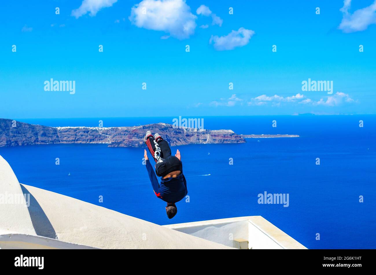 La espalda de un joven atleta se voltea durante el Parkour y el Free Running. Atleta profesional que realiza un backflip en un techo en Santorini, Isla, Grecia, Europa. Foto de stock