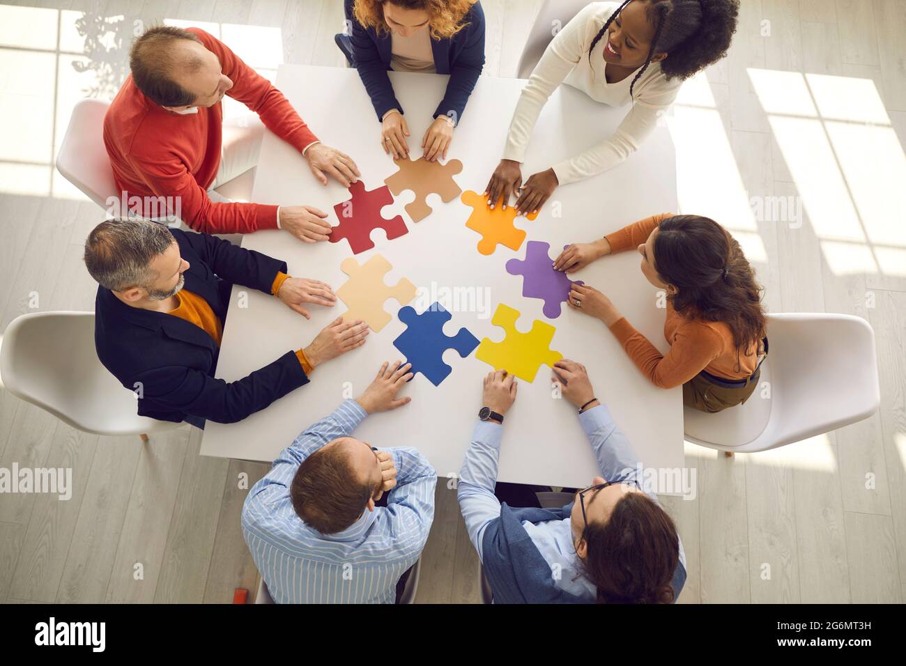 Equipo de negocios creativo sentado alrededor de la mesa de la oficina y tratando de poner piezas de rompecabezas juntos Foto de stock