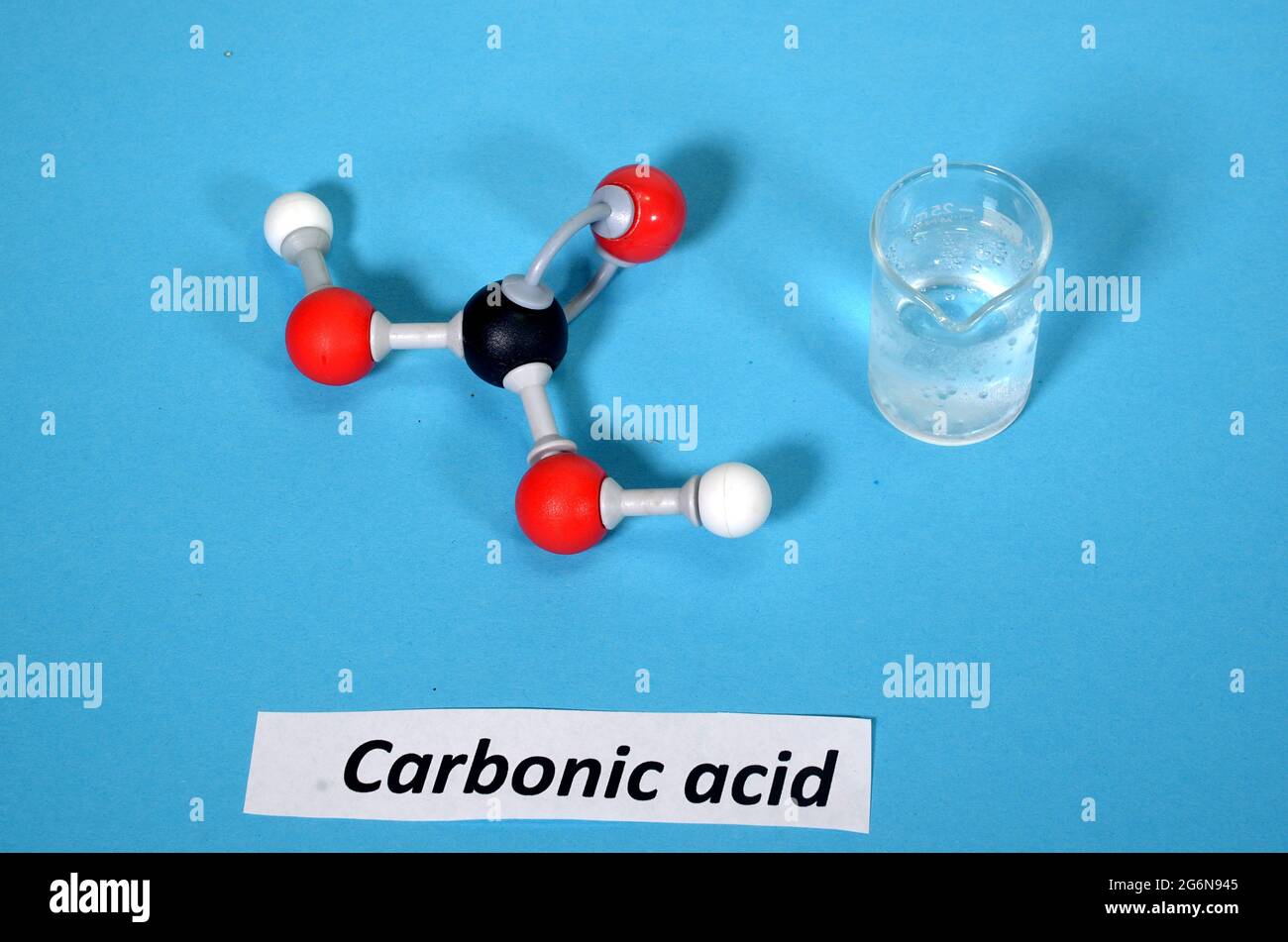 Modelo de molécula de ácido carbónico junto con la muestra en un vaso de precipitados. El blanco es hidrógeno, el negro es carbono y el rojo es oxígeno. Foto de stock