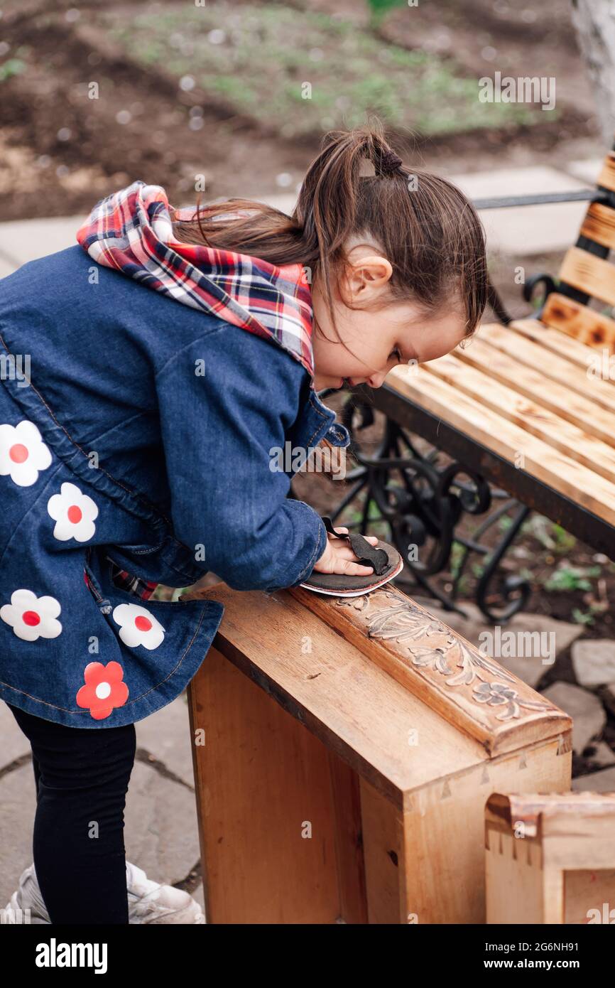 una niña ayuda a lijar una vieja caja de cajones de madera con un rollo de  papel de lija, reciclando muebles antiguos Fotografía de stock - Alamy